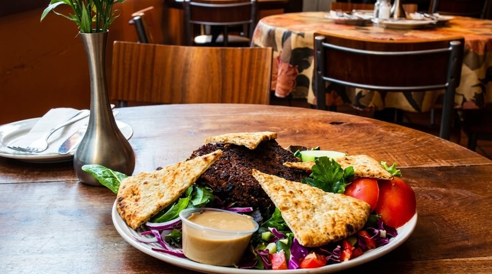 A plate of grilled meat, pita bread, salad, and dipping sauce on a wooden restaurant table.