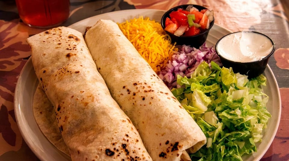 Two burritos with shredded cheese, lettuce, diced onions, pico de gallo, and sour cream.