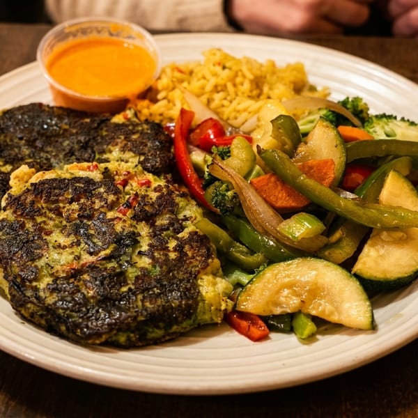 A plate of vegetable fritters, yellow rice, and sautéed mixed vegetables with a side of orange sauce.
