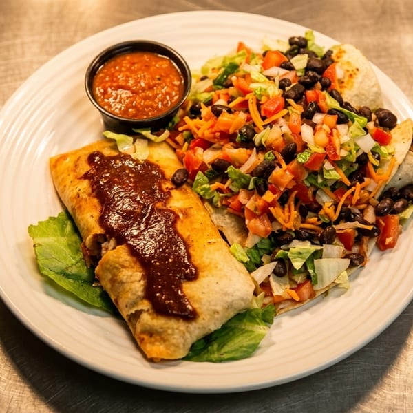A plate of two burritos, one topped with sauce, served with a side salad and salsa.